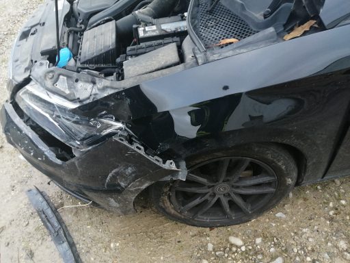 Schwarzes Auto mit beschädigter Front und zerkratztem Kotflügel.