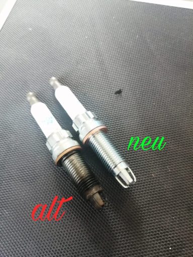 Zwei Zündkerzen, eine alte und eine neue, nebeneinander auf schwarzem Untergrund.